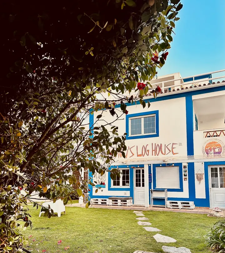 Captain's Log House garden facade with blue trim and camellia tree in bloom